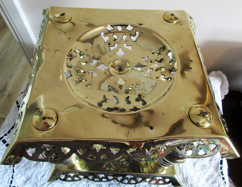 A square two-tier Victorian brass trivet stand featuring pierced fretwork surfaces and turned baluster column supports. View II
