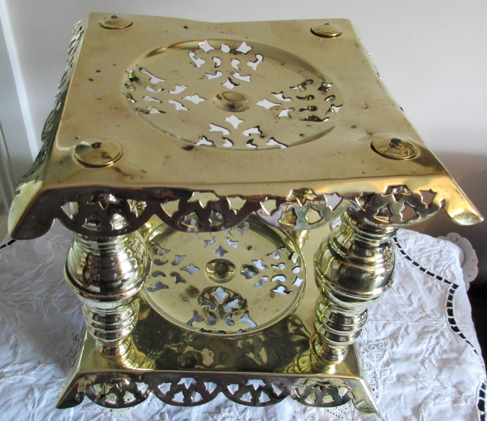 A square two-tier Victorian brass trivet stand featuring pierced fretwork surfaces and turned baluster column supports. View VI