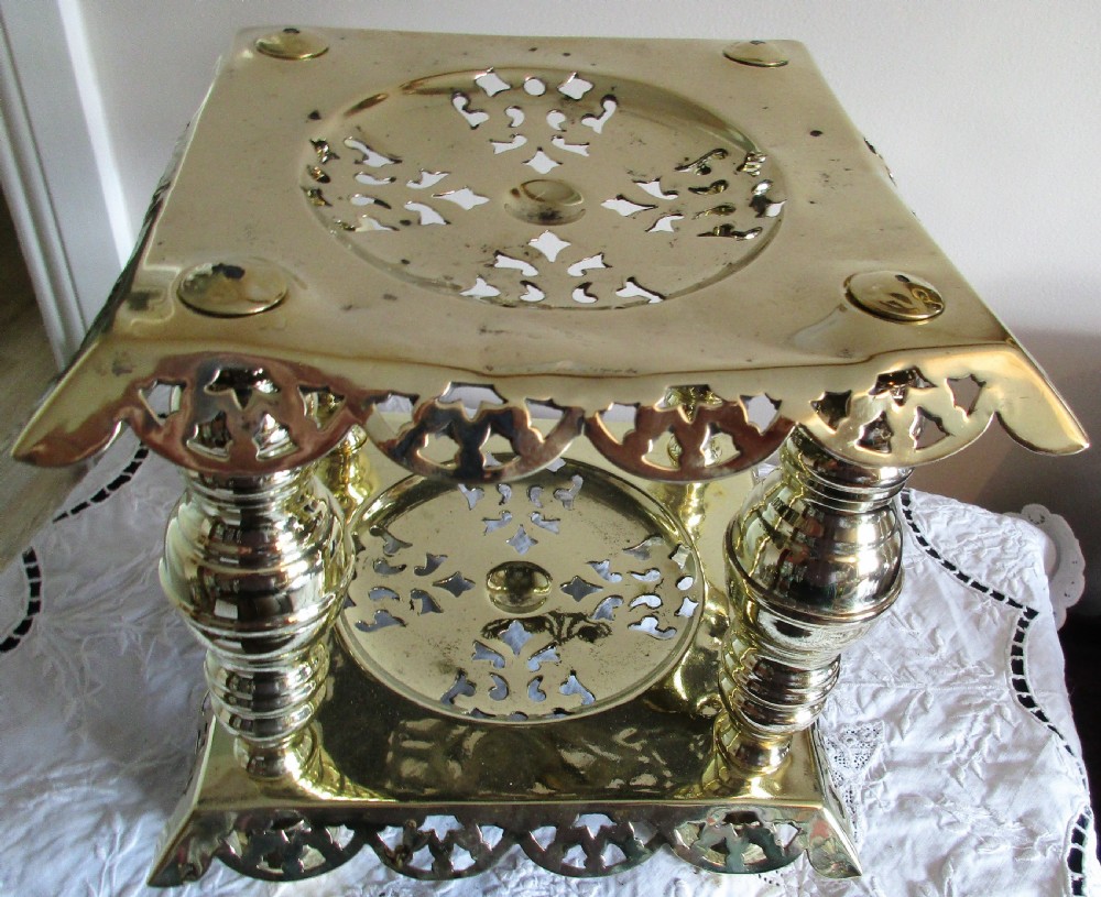 A square two-tier Victorian brass trivet stand featuring pierced fretwork surfaces and turned baluster column supports. View VII