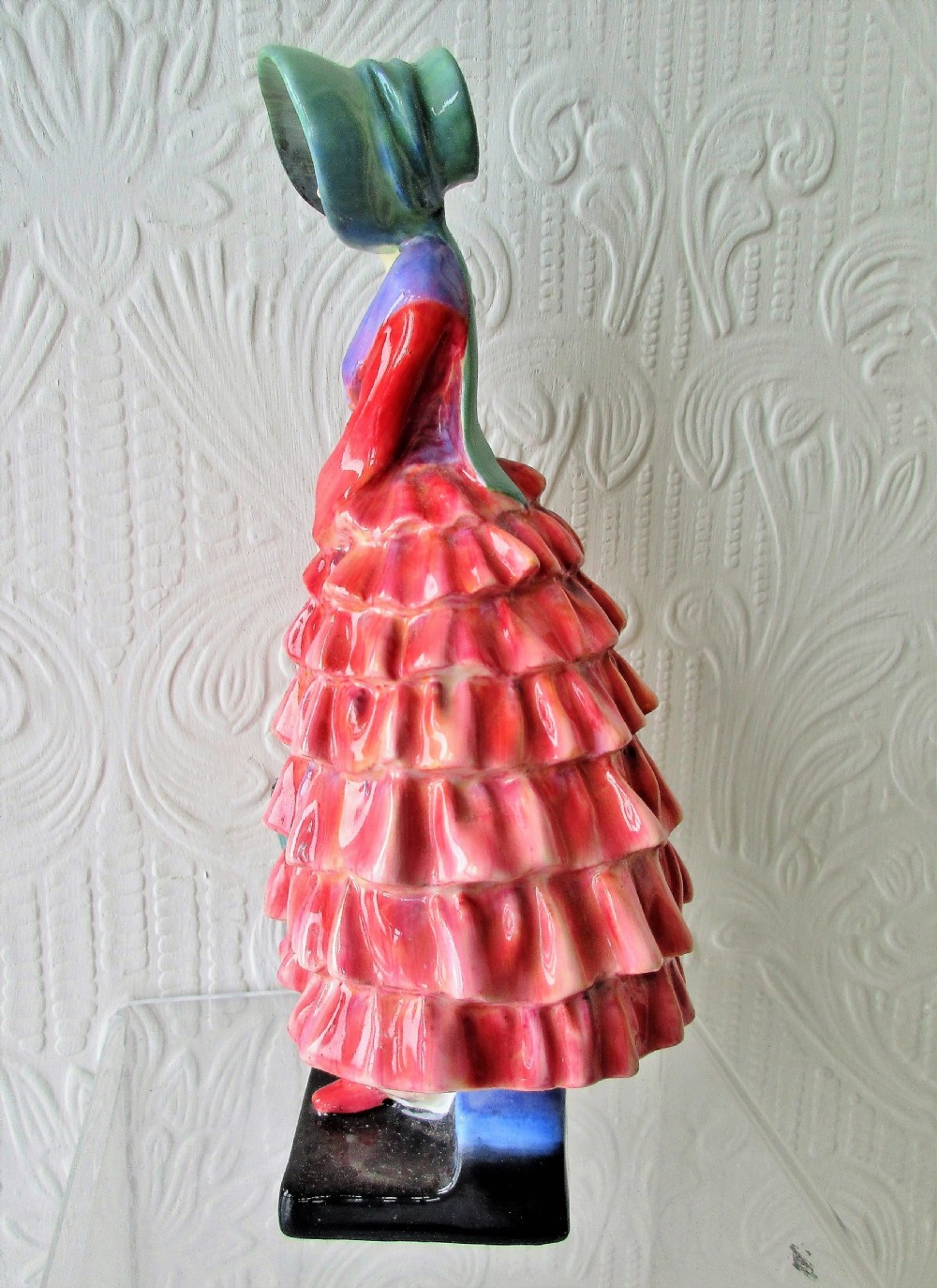 A Royal Doulton porcelain figurine titled Priscilla depicting a lady in a red tiered dress and green bonnet holding a parasol. View II
