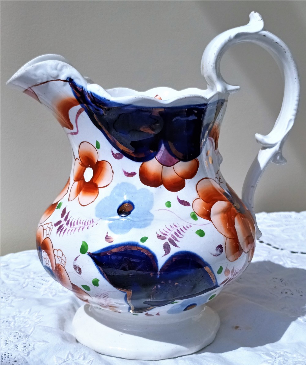 A Victorian Gaudy Welsh pottery jug featuring hand-painted cobalt blue and orange floral motifs with copper lustre accents and an ornate white handle.