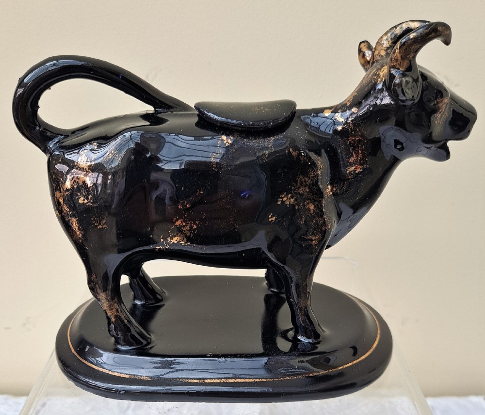 A Victorian Jackfield black-glazed ceramic cow creamer featuring gilded detailing and mounted on a contoured oval base. View III