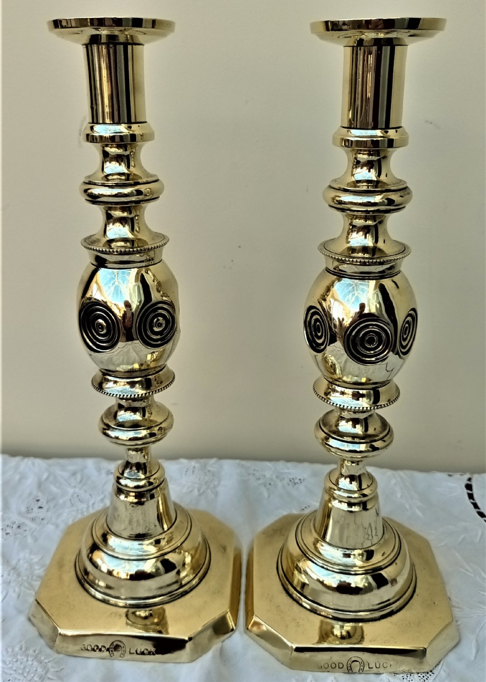 A pair of polished Victorian brass candlesticks featuring turned stems with concentric circle motifs and octagonal bases stamped with good luck text.