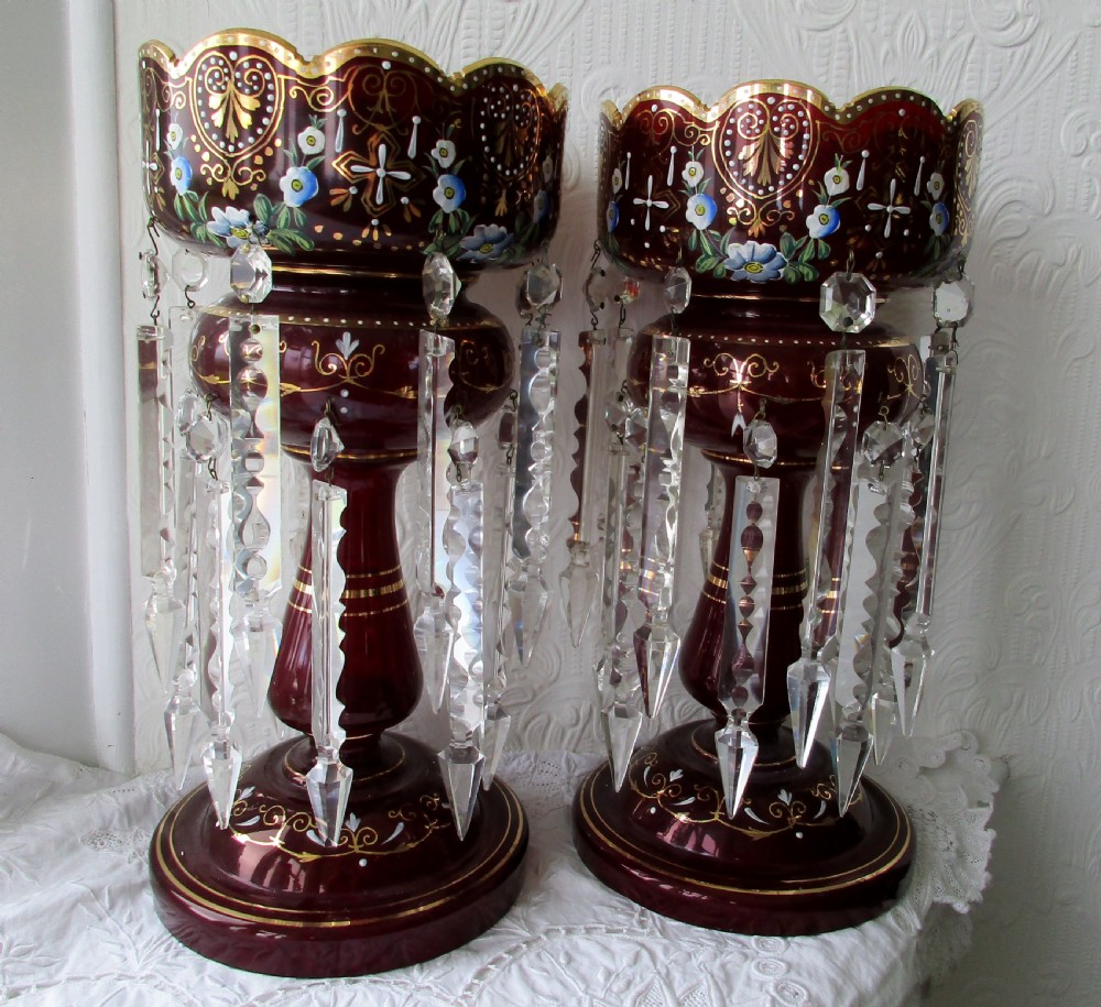A pair of Victorian ruby glass lustres featuring hand-painted floral enamelling, gilt accents, and hanging clear crystal prisms.