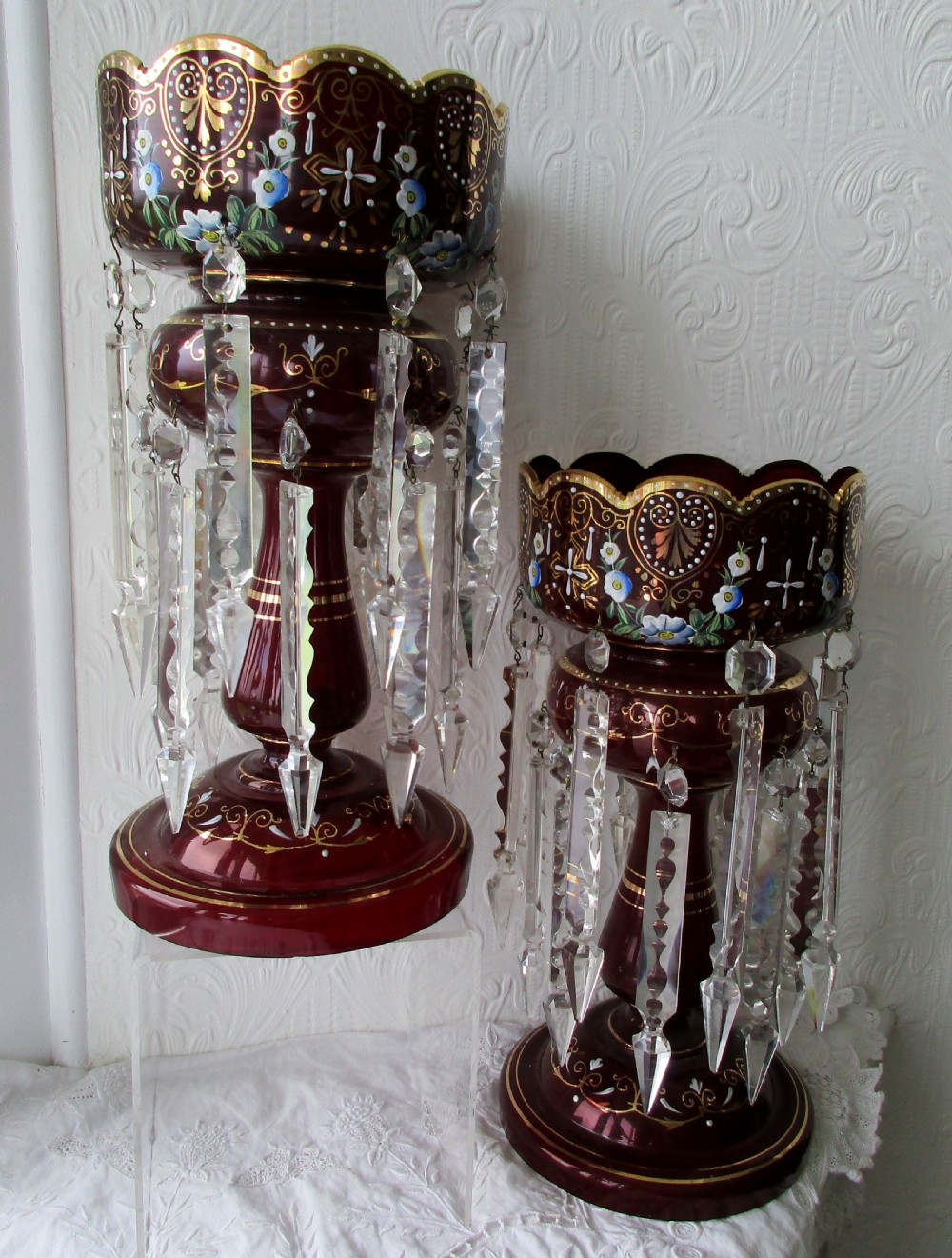 A pair of Victorian ruby glass lustres featuring hand-painted floral enamelling, gilt accents, and hanging clear crystal prisms. View V