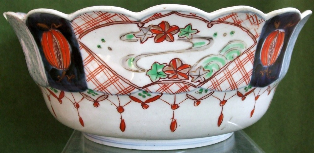 An antique Japanese Imari porcelain bowl featuring a scalloped rim, hand-painted cobalt blue and iron-red panelled motifs, and a central pine landscape. View II