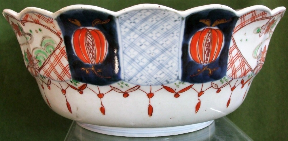 An antique Japanese Imari porcelain bowl featuring a scalloped rim, hand-painted cobalt blue and iron-red panelled motifs, and a central pine landscape. View III