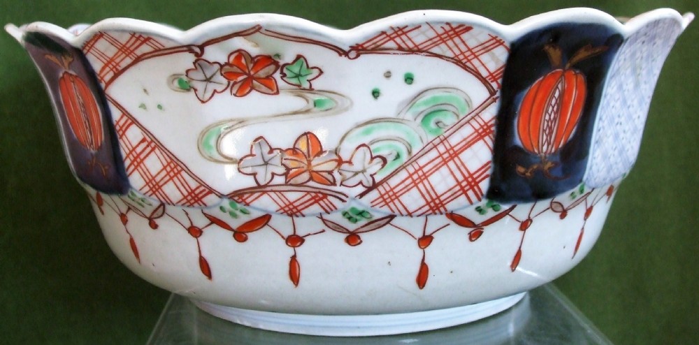 An antique Japanese Imari porcelain bowl featuring a scalloped rim, hand-painted cobalt blue and iron-red panelled motifs, and a central pine landscape. View IV