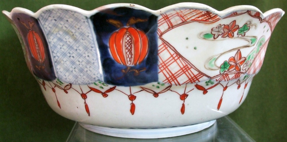 An antique Japanese Imari porcelain bowl featuring a scalloped rim, hand-painted cobalt blue and iron-red panelled motifs, and a central pine landscape. View V