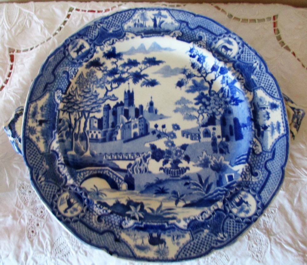 An antique Georgian circular blue and white transferware hot-water plate with side handles featuring a central Gothic castle scene and ornate border.