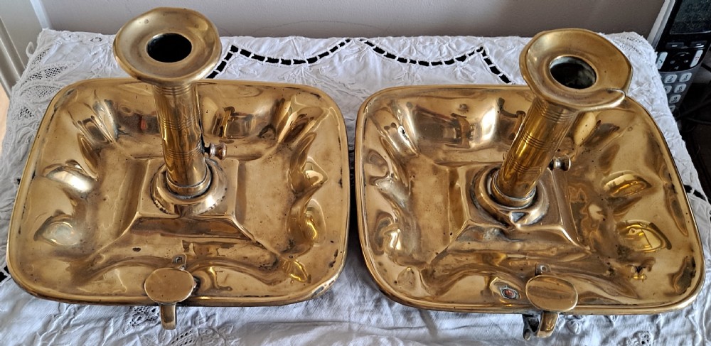 A pair of Victorian polished brass chambersticks with square dished trays, central socket columns, and side thumb handles. View II