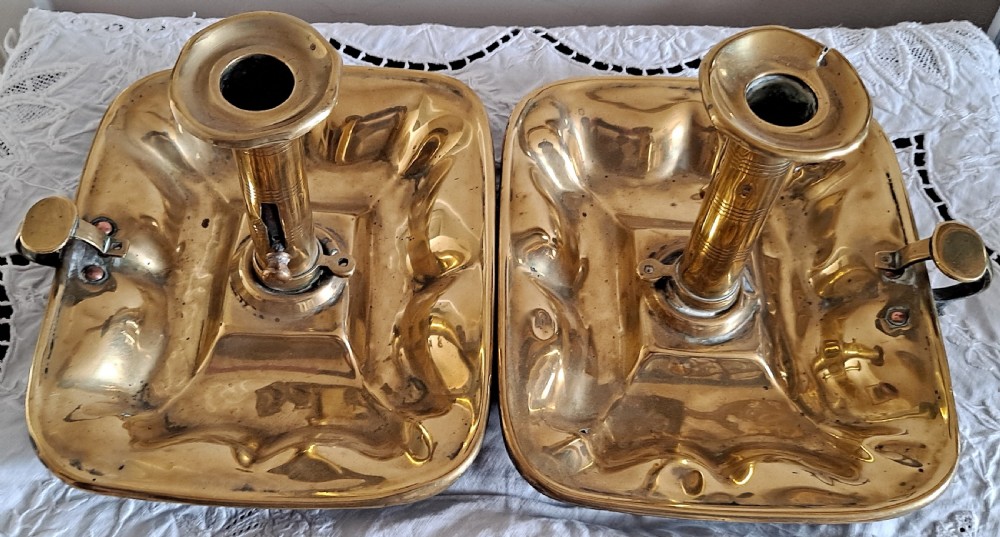 A pair of Victorian polished brass chambersticks with square dished trays, central socket columns, and side thumb handles. View III