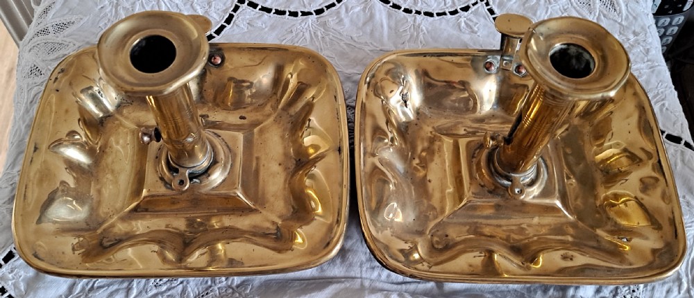 A pair of Victorian polished brass chambersticks with square dished trays, central socket columns, and side thumb handles. View IV