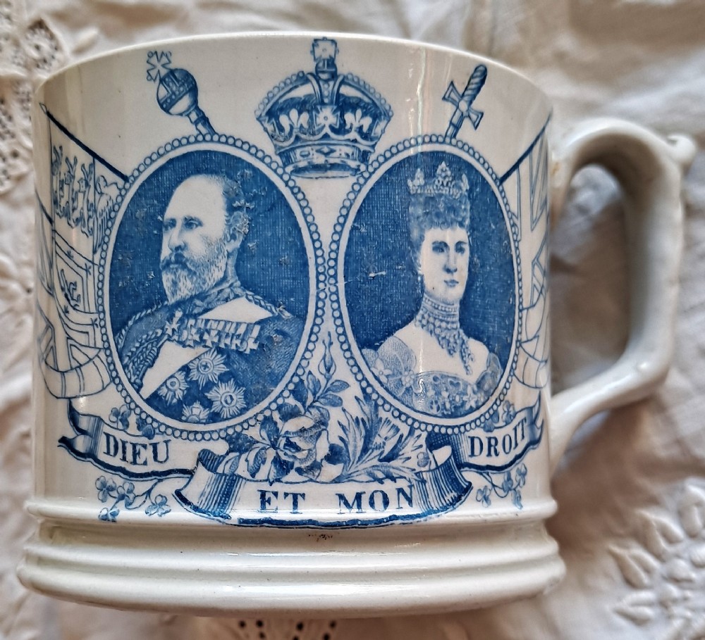 A white ceramic mug decorated with blue transfer-printed portraits of King Edward VII and Queen Alexandra alongside heraldic emblems.