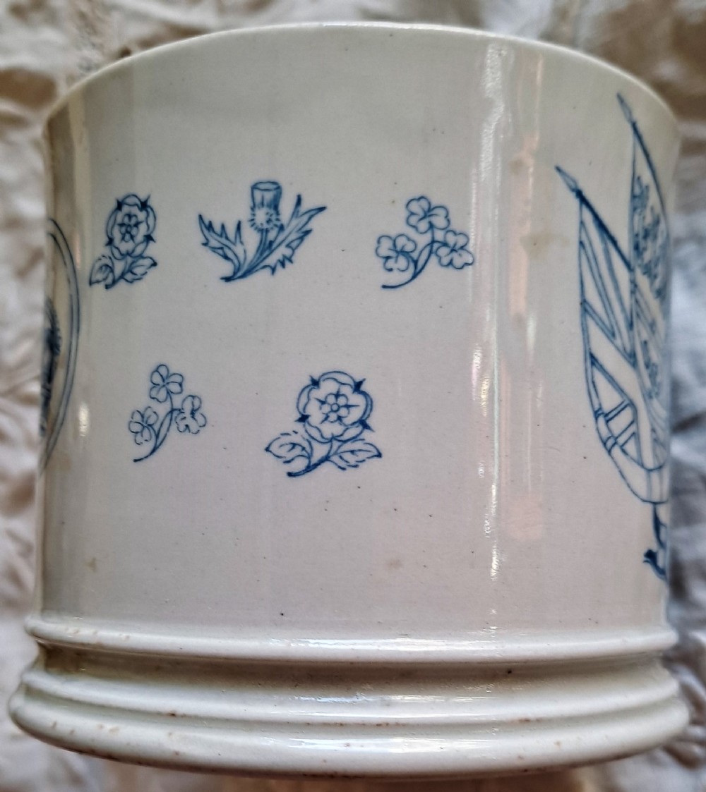 A white ceramic mug decorated with blue transfer-printed portraits of King Edward VII and Queen Alexandra alongside heraldic emblems. View II