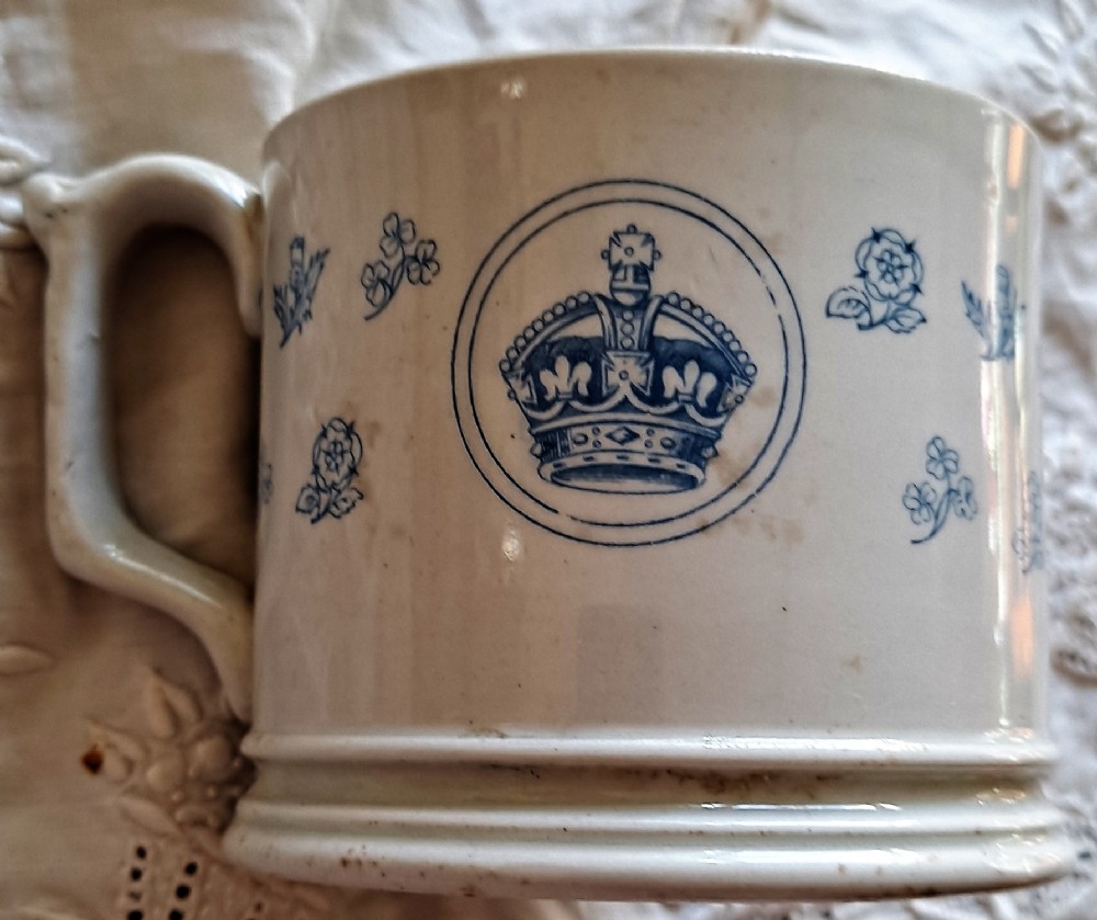 A white ceramic mug decorated with blue transfer-printed portraits of King Edward VII and Queen Alexandra alongside heraldic emblems. View III