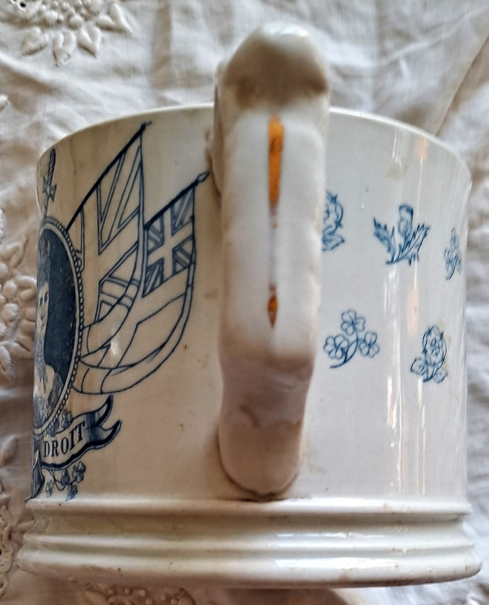 A white ceramic mug decorated with blue transfer-printed portraits of King Edward VII and Queen Alexandra alongside heraldic emblems. View IV