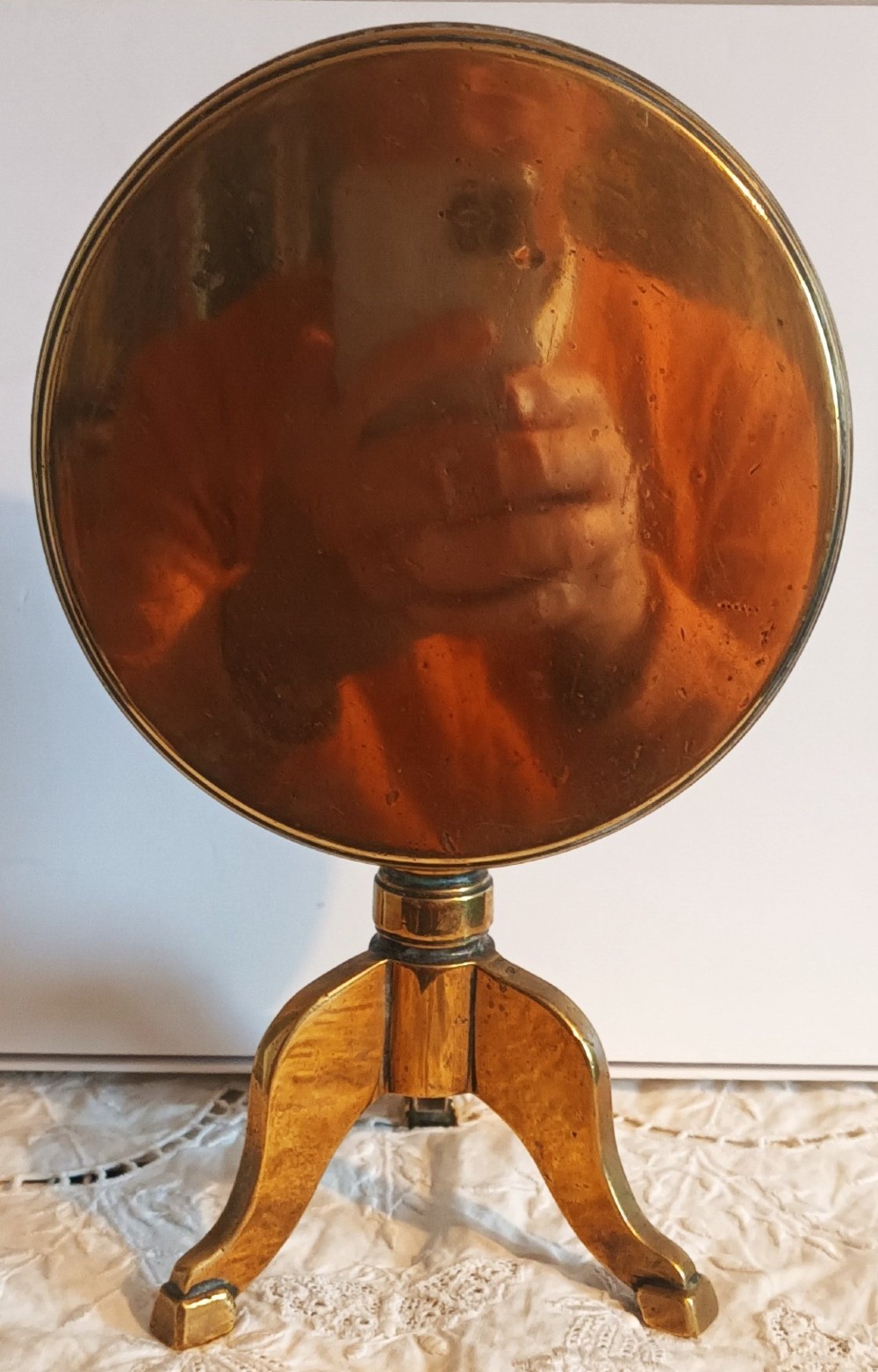 An antique Georgian brass candle reflector featuring a polished circular disc set on a turned column with a tripod base. View II