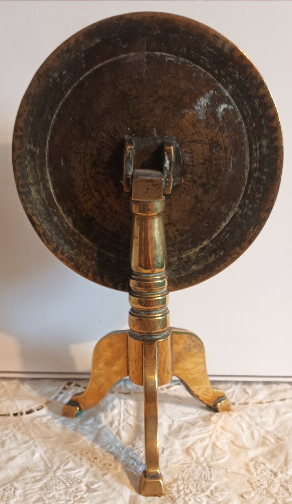 An antique Georgian brass candle reflector featuring a polished circular disc set on a turned column with a tripod base. View IV