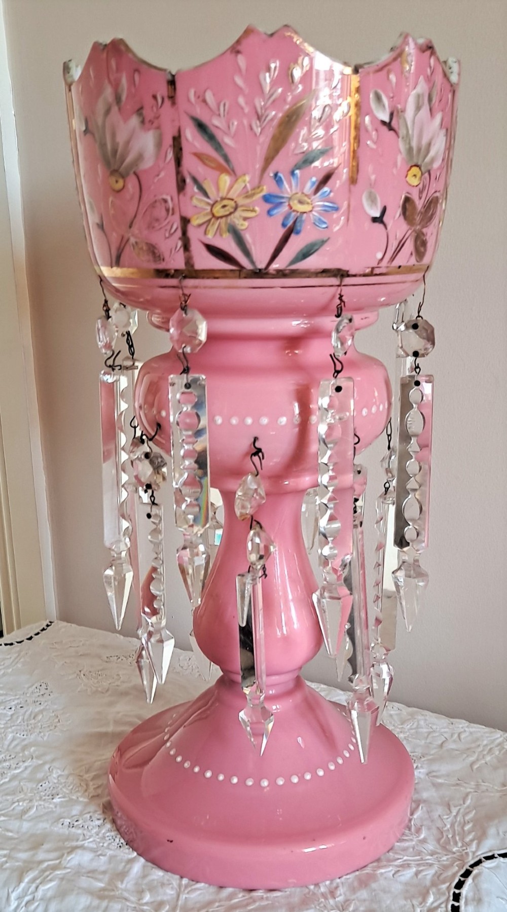 A Victorian pink glass mantel lustre featuring hand-painted floral enamel details, gilt trimming, a castellated top, and hanging clear cut-crystal prisms. View V