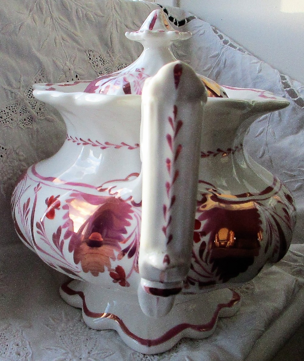 An antique white porcelain teapot decorated with pink iridescent metallic leaf motifs, a scalloped base, curved spout, and molded finial lid. View II