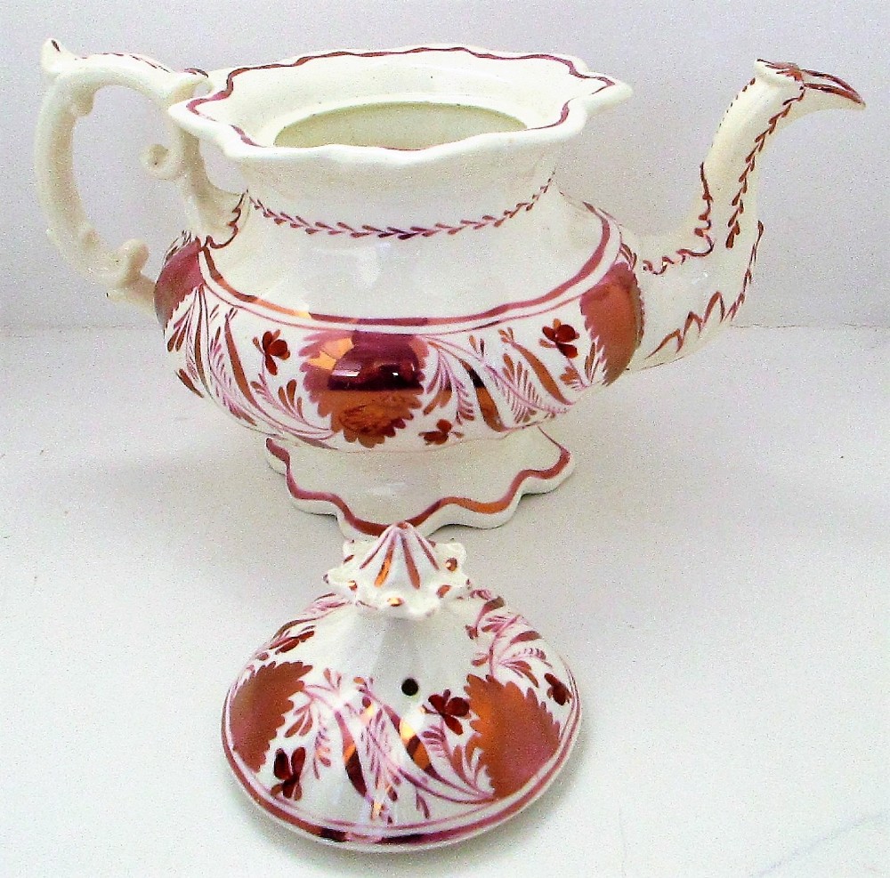 An antique white porcelain teapot decorated with pink iridescent metallic leaf motifs, a scalloped base, curved spout, and molded finial lid. View VII