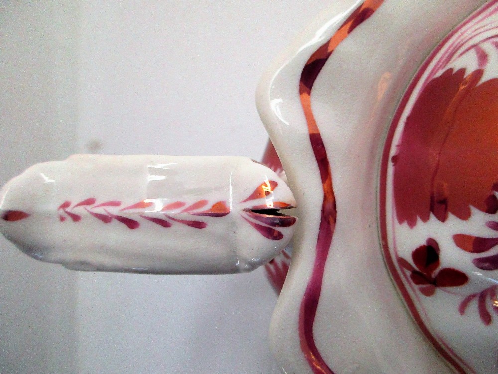 An antique white porcelain teapot decorated with pink iridescent metallic leaf motifs, a scalloped base, curved spout, and molded finial lid. View X