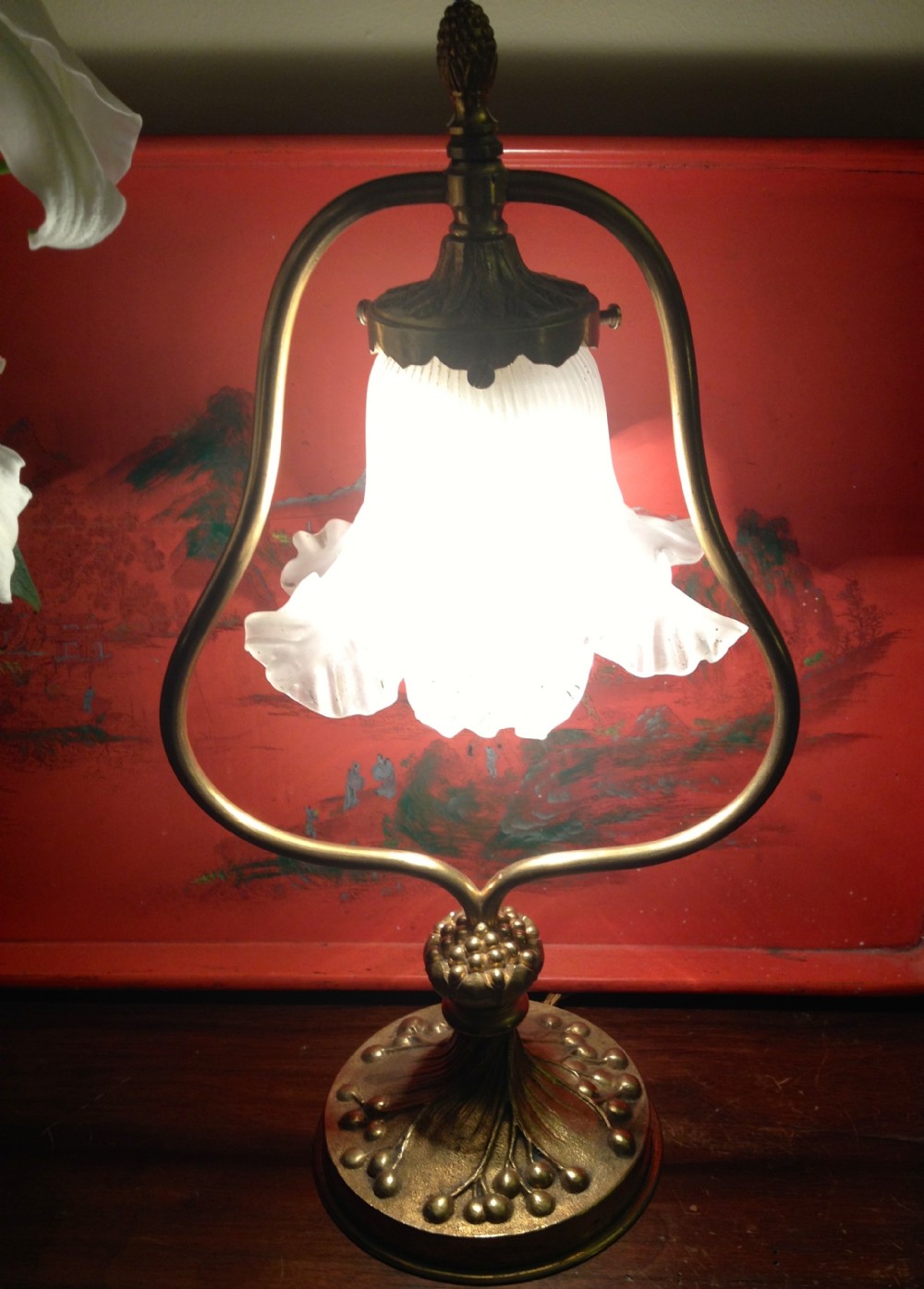 An Art Nouveau style gilt bronze desk lamp featuring a floral cast base, a curved loop frame, and a frilled frosted glass shade.