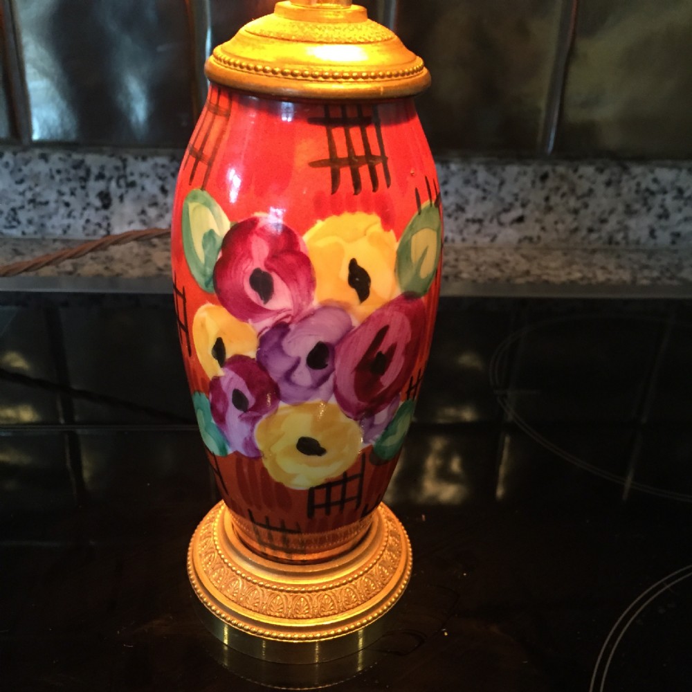 A hand-painted Art Deco faience ceramic table lamp featuring red, purple, and yellow floral patterns mounted on a textured brass base.