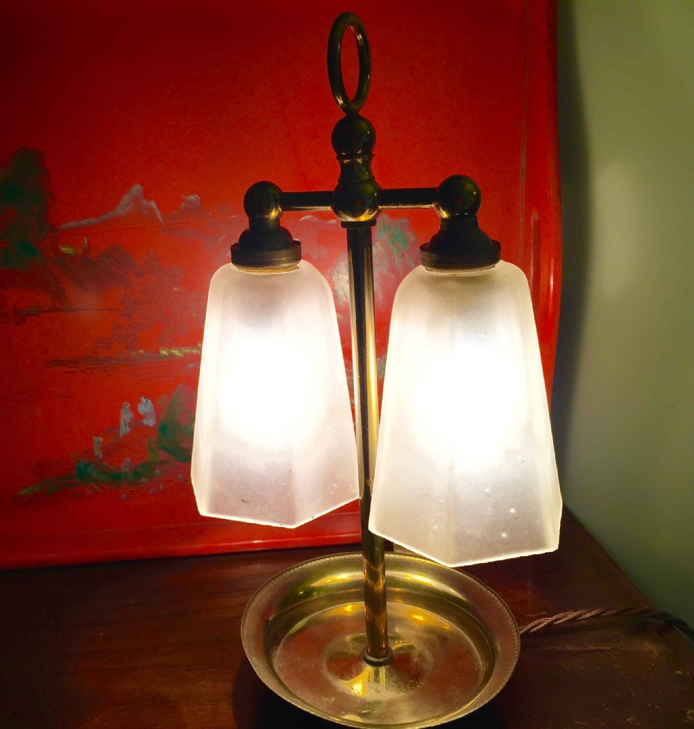 An Art Deco brass table lamp featuring twin arms with tapered frosted glass shades and a central loop handle above a dished base.