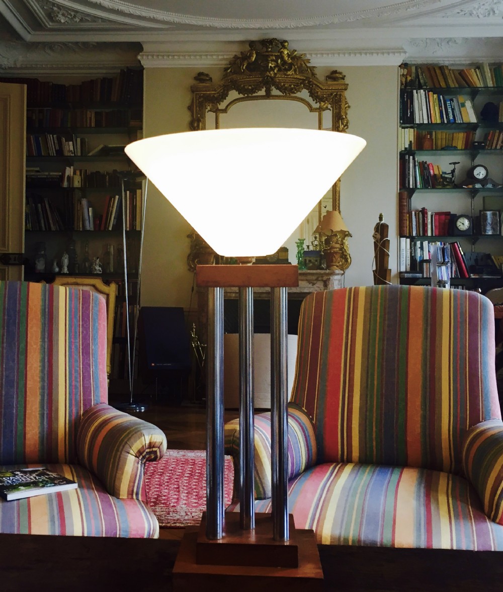 A tall modernist table lamp featuring a conical white opaline glass shade supported by three chrome tubular columns on a rectangular wooden base.