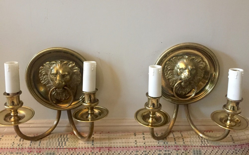 A pair of 19th-century French cast brass wall sconces featuring oval backplates with detailed lion heads holding rings and twin curved candle arms. View VII