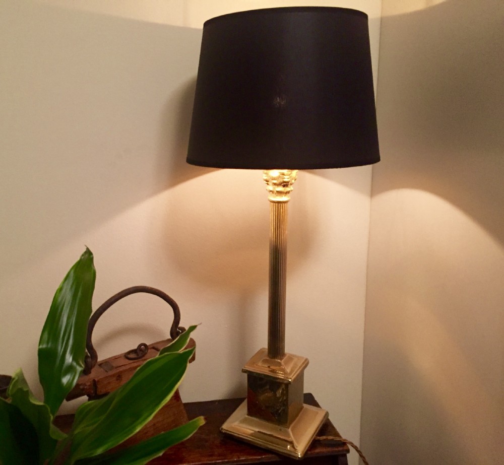 An Edwardian brass desk lamp featuring a fluted column stem on a stepped square plinth base, fitted with a black drum lampshade.
