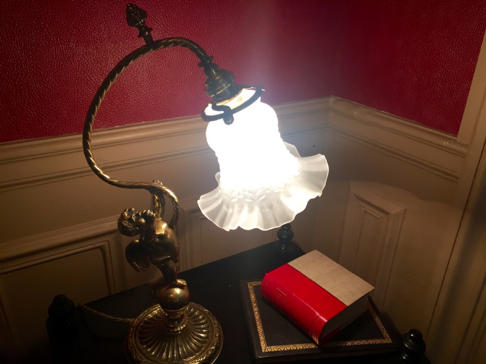 An antique brass and bronze table lamp featuring a cherub figure supporting a twisted gooseneck arm with a ribbed frosted glass shade. View IV
