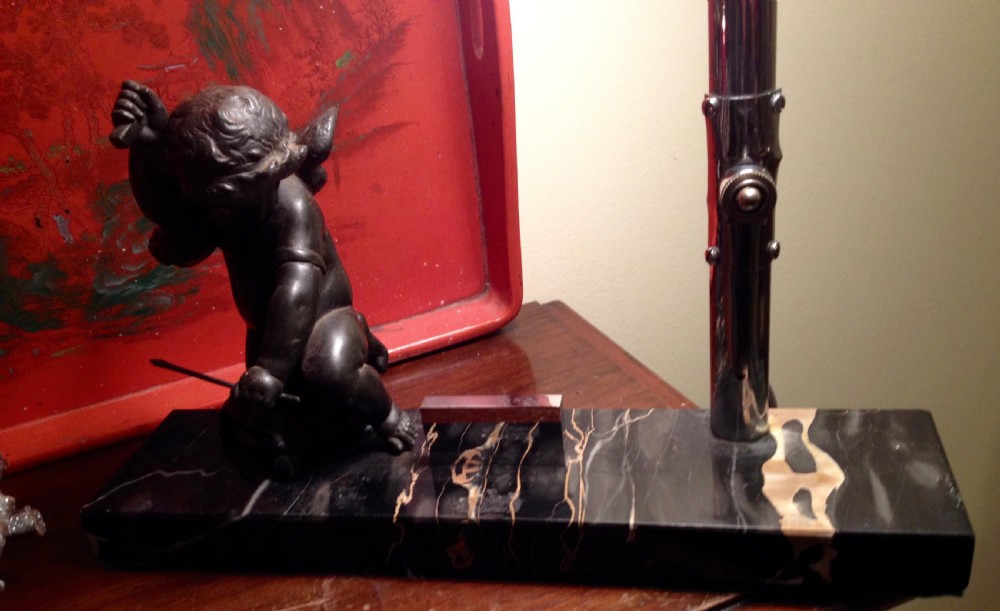 An Art Deco table lamp featuring a white glass flared shade on a chrome stem, mounted on a veined black marble base beside a small metal figure. View V