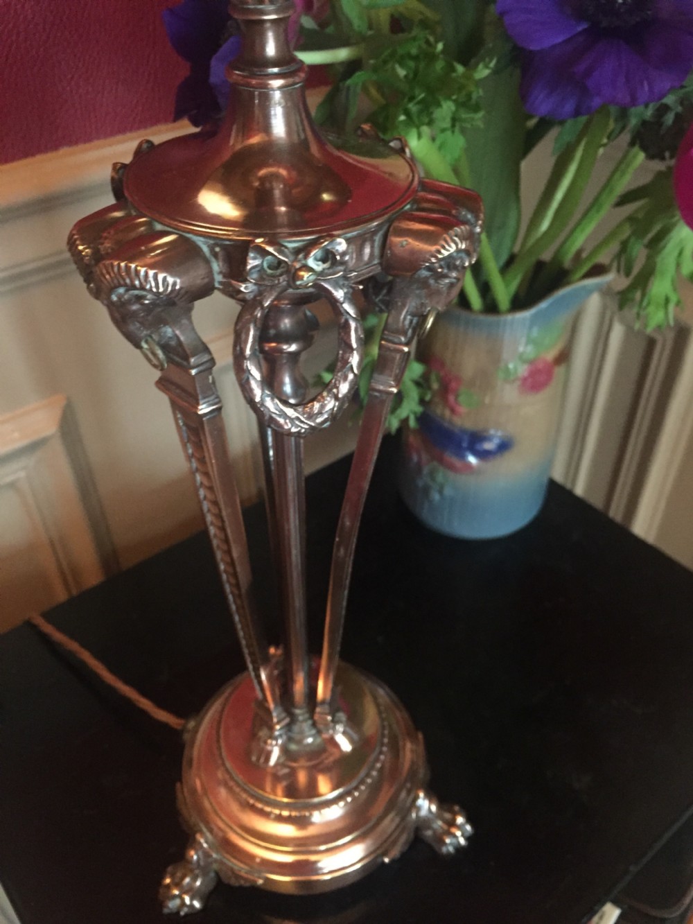 A French Empire style gilt metal table lamp base featuring three tripod legs decorated with rams heads, laurel wreaths, and claw feet. View V