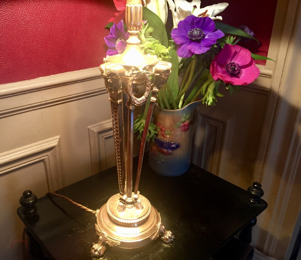 A French Empire style gilt metal table lamp base featuring three tripod legs decorated with rams heads, laurel wreaths, and claw feet. View XI