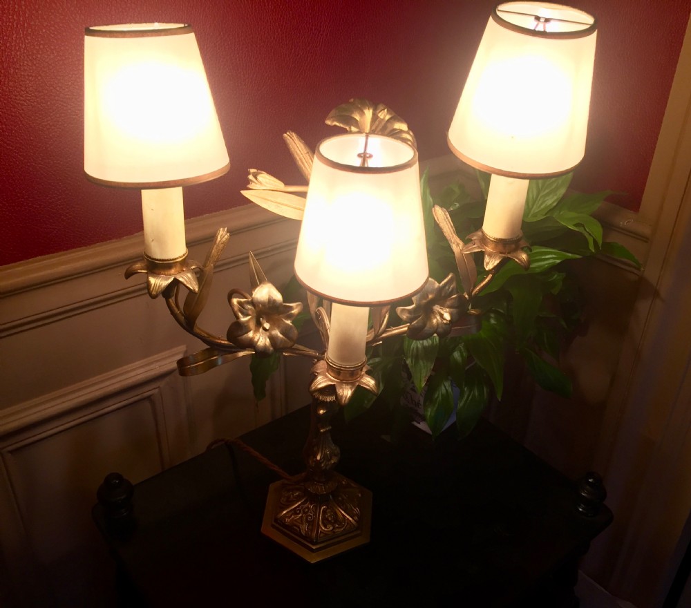 A 1920s French gilt brass three-arm candelabra table lamp featuring botanical leaf and blossom motifs with neutral fabric shades. View V