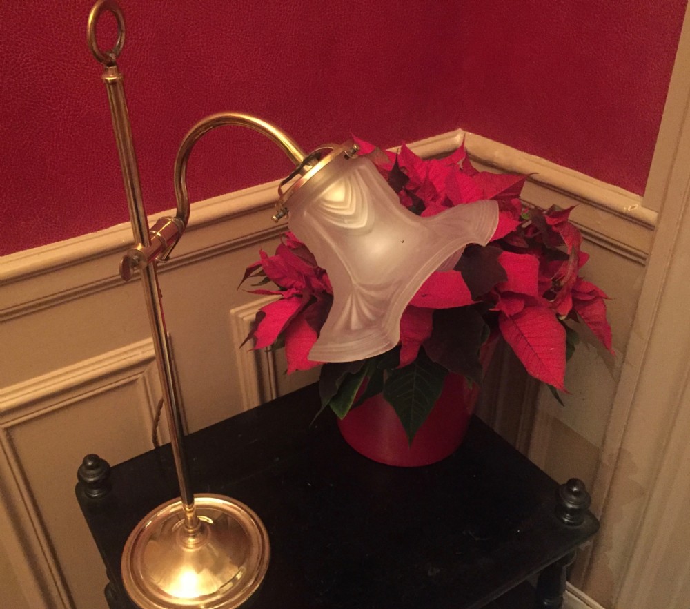 An Edwardian brass desk lamp featuring a circular base, an adjustable vertical stem, and a frosted, flared glass shade.