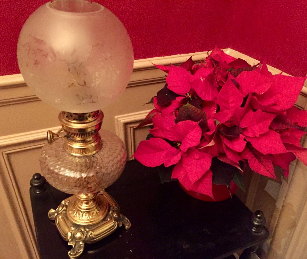 An Art Nouveau table lamp featuring an ornate cast brass base, a clear patterned glass reservoir, and a frosted spherical glass shade.
