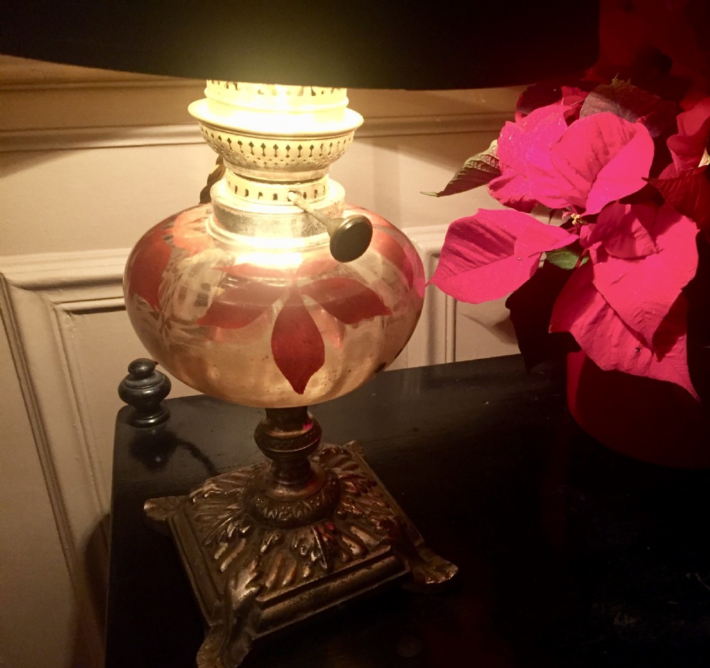 An antique Art Nouveau converted oil lamp featuring a cast metal base, a clear glass font with red enamelled leaf motifs, and a brass gallery. View V