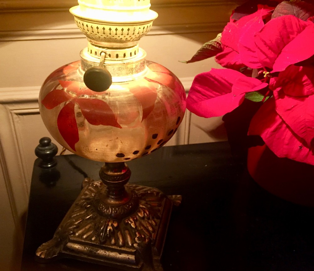 An antique Art Nouveau converted oil lamp featuring a cast metal base, a clear glass font with red enamelled leaf motifs, and a brass gallery.