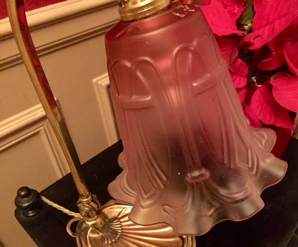 An Edwardian adjustable brass desk lamp featuring a shell-shaped base, a curved arm, and an illuminated fluted cranberry pink glass shade. View VI