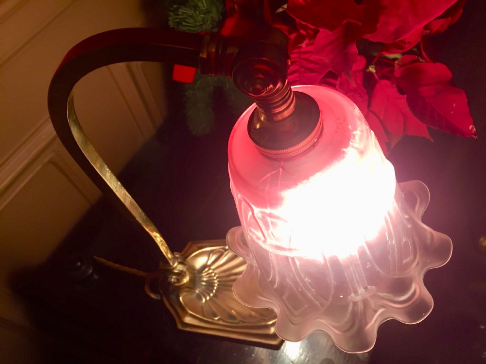 An Edwardian adjustable brass desk lamp featuring a shell-shaped base, a curved arm, and an illuminated fluted cranberry pink glass shade. View IX