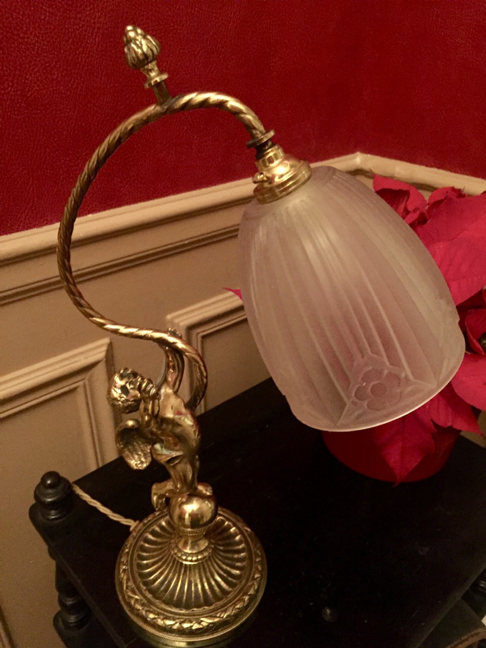 An antique brass and bronze table lamp featuring a cherub figure supporting a twisted gooseneck arm with a ribbed frosted glass shade.