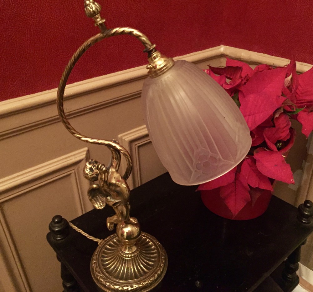 An antique brass and bronze table lamp featuring a cherub figure supporting a twisted gooseneck arm with a ribbed frosted glass shade. View X