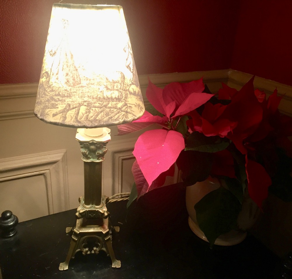An antique French bronze column table lamp featuring a fluted shaft and Corinthian capital topped with a Toile de Jouy patterned shade.
