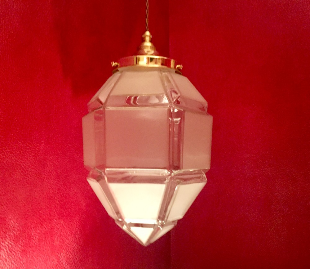 An Art Deco geometric faceted frosted glass pendant light featuring a brass gallery top and pointed lower tip.