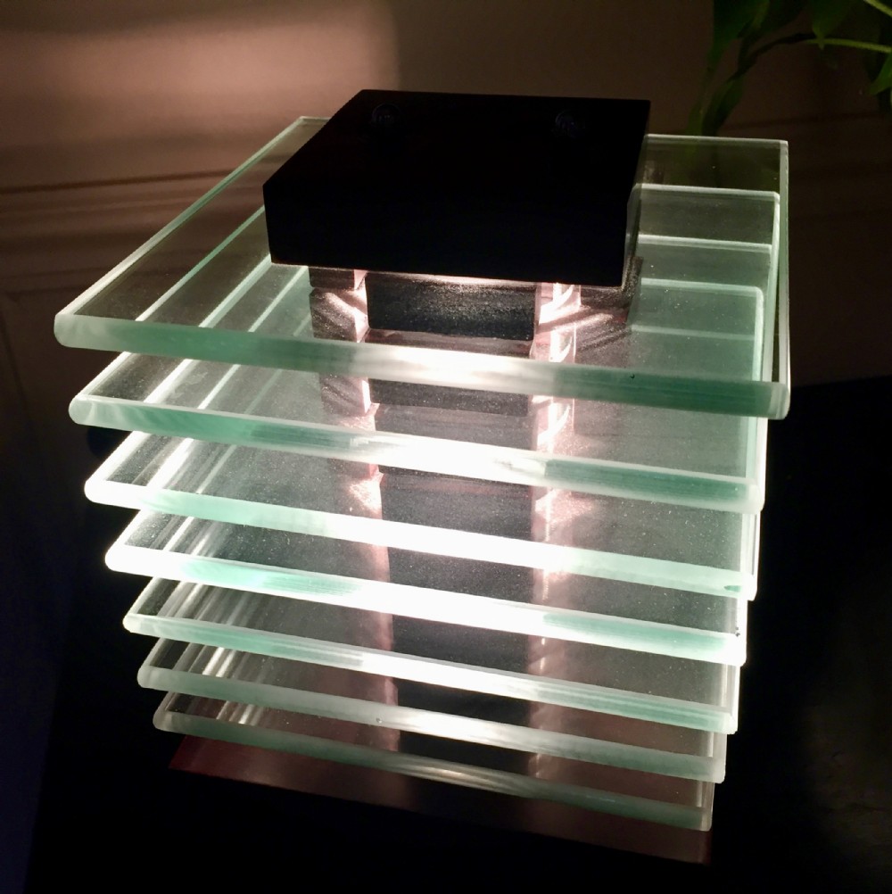 A modernist cubic table lamp constructed from horizontal stacked square glass plates topped with a dark mahogany cap.