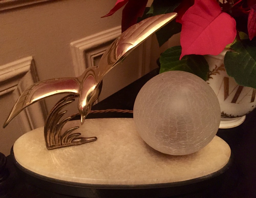 An Art Deco night light featuring a polished brass seagull sculpture and a frosted spherical glass shade mounted on an oval marble base.